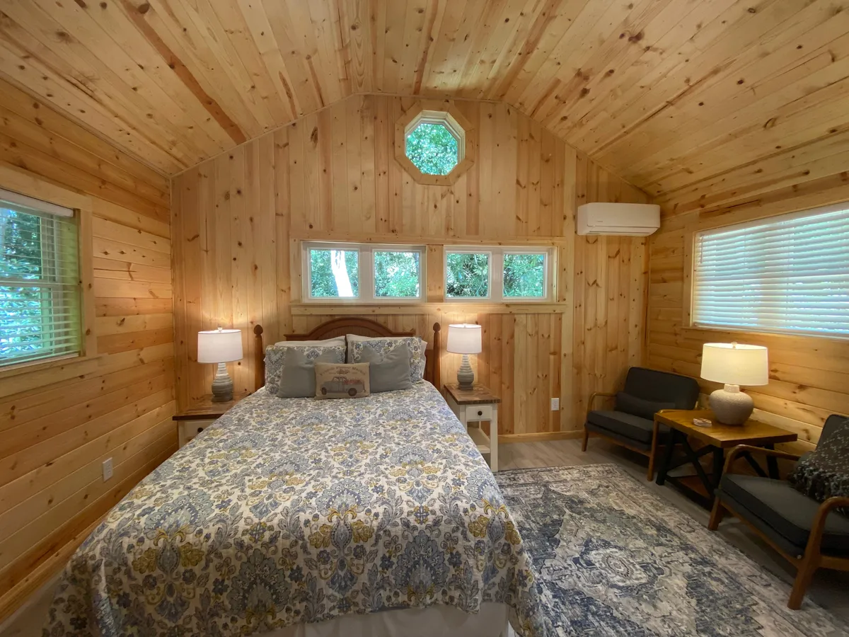 This interior scene centers on a bed with decorative bedding flanked by two bedside lamps, complemented by a small seating area with comfortable chairs. Natural light bathes the space, emphasizing its serene and comforting mood.